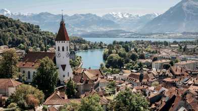 A scenic view of Thun, Switzerland, with a church tower, a lake, and mountains in the background, where the seminar was held.