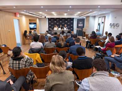 A picture from behind of people sitting in a room facing discussants at the Policy Forum
