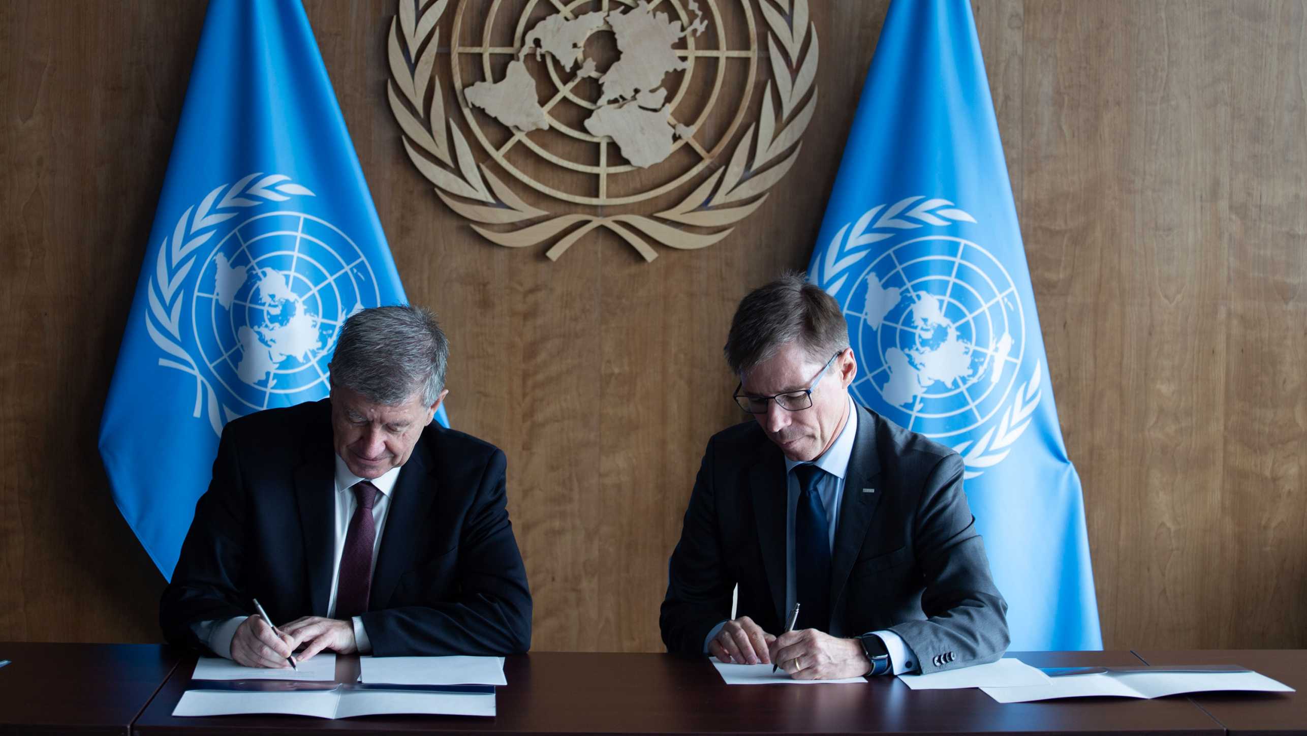 UNO-Untergeneralsekretär Guy Ryder und ETH-Präsident Joël Mesot bei der Unterzeichnung einer Absichtserklärung im Oktober 2023, an einem Tisch sitzend, hinter ihnen zwei Fahnen der Vereinten Nationen und das UNO-Emblem an der Wand.