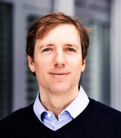 Portrait of Prof. Dominik Hangartner with a blue shirt smiling at the camera