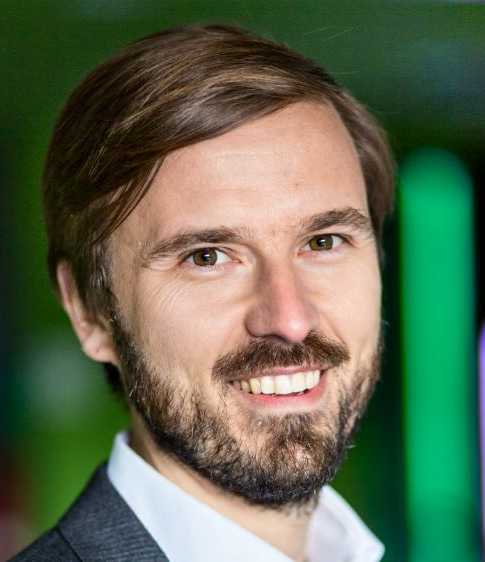 Portrait of Prof. Tobias Schmidt with short light brown hair, wearing a dark grey suit, white shirt, smiling at the camera.