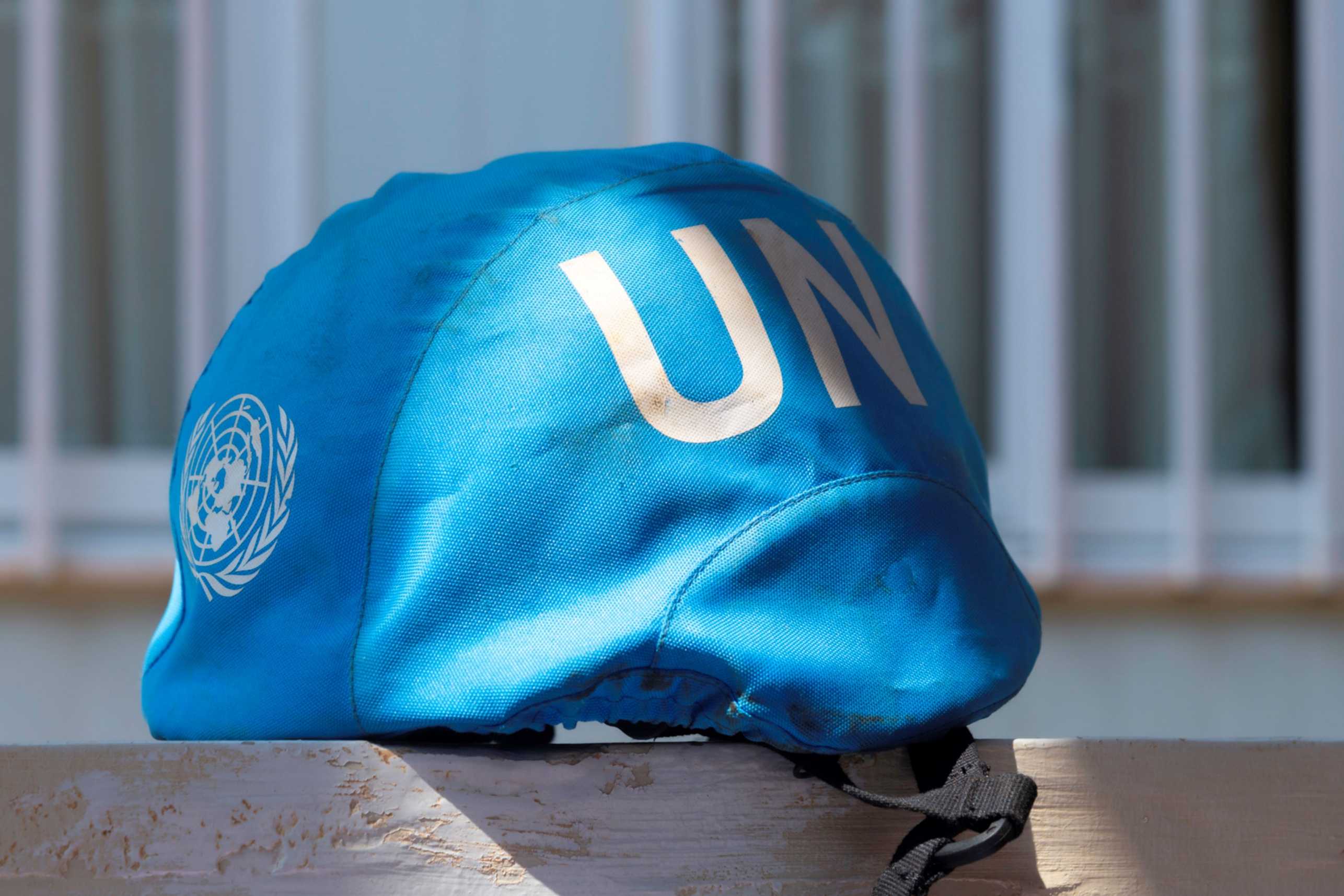 Blue United Nations helmet with 'UN' written in white letters, symbolizing peacekeeping efforts, resting on a surface in front of a building.