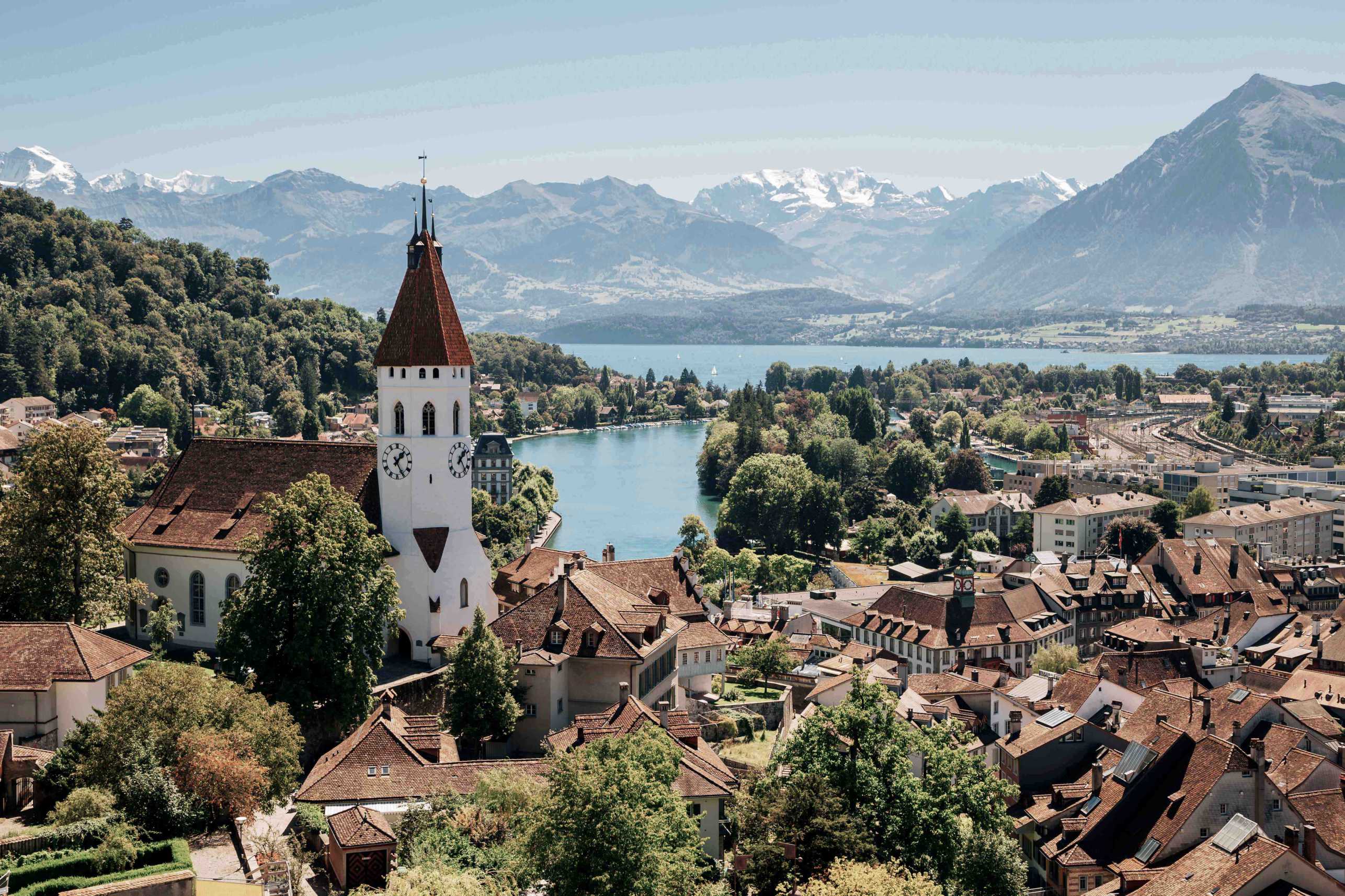 A scenic view of Thun, Switzerland, with a church tower, a lake, and mountains in the background