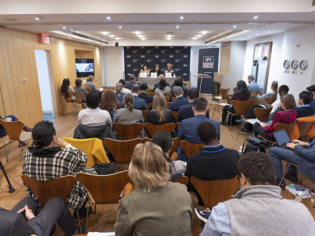 A picture from behind of people sitting in a room facing discussants at the Policy Forum