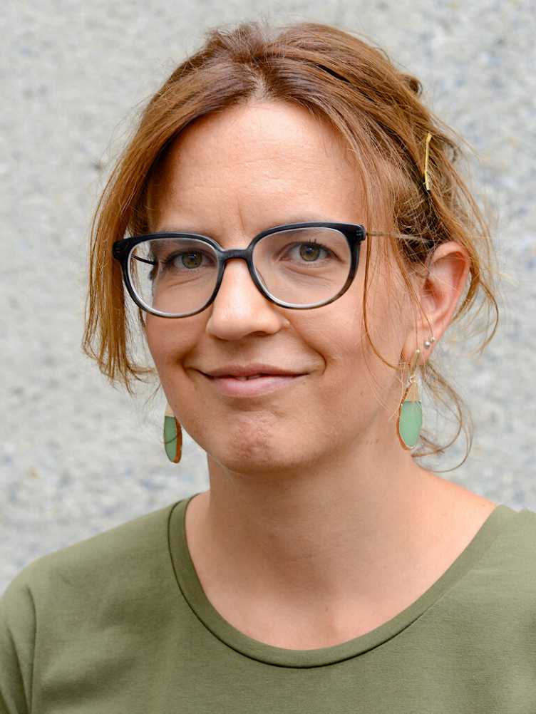 Portrait of Prof. Günther Isabel with light brown hair, wearing glasses, green earrings, and a green top, smiling softly at the camera.